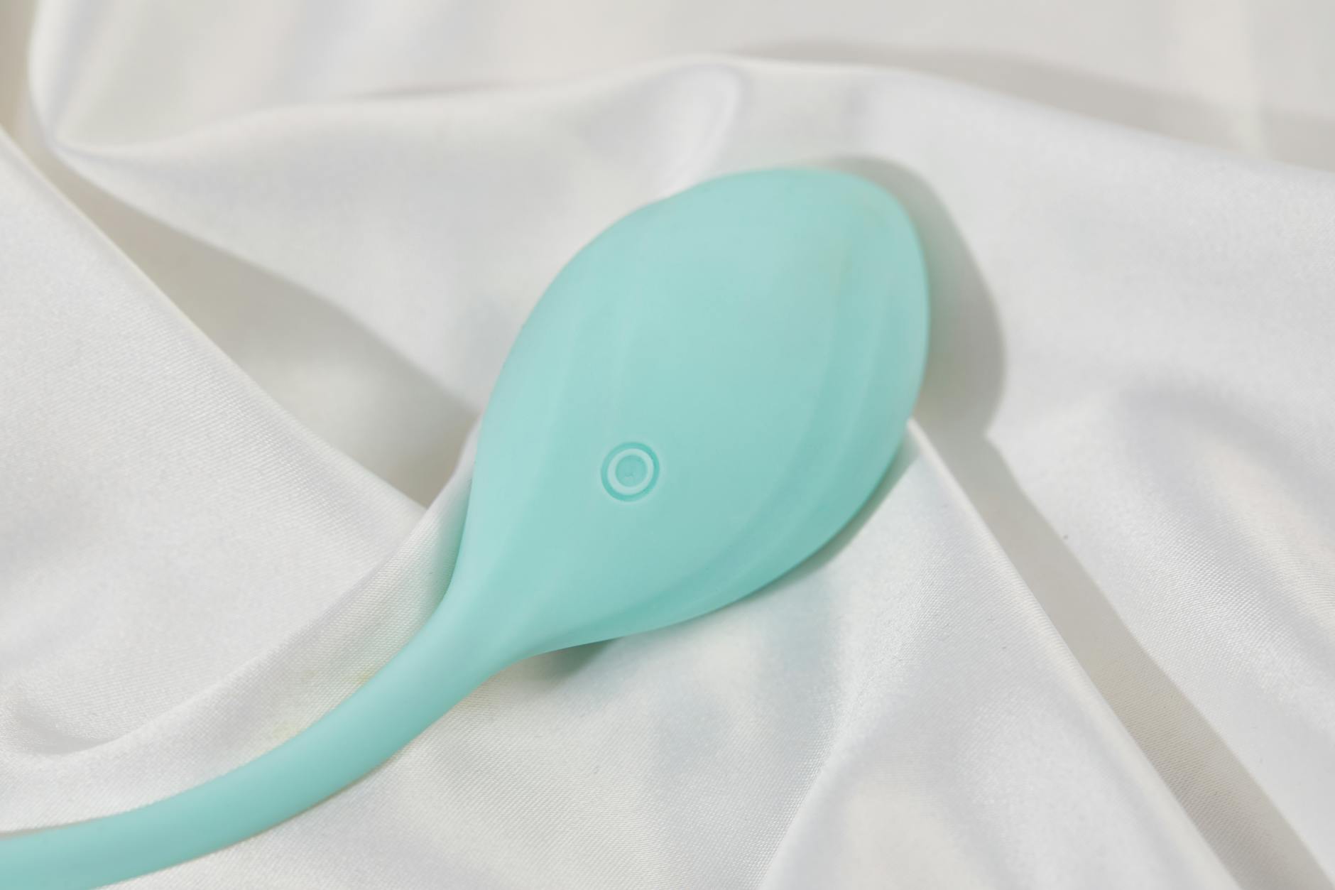 A stylish teal vibrator on smooth white silk fabric, perfect for modern intimate wellness.