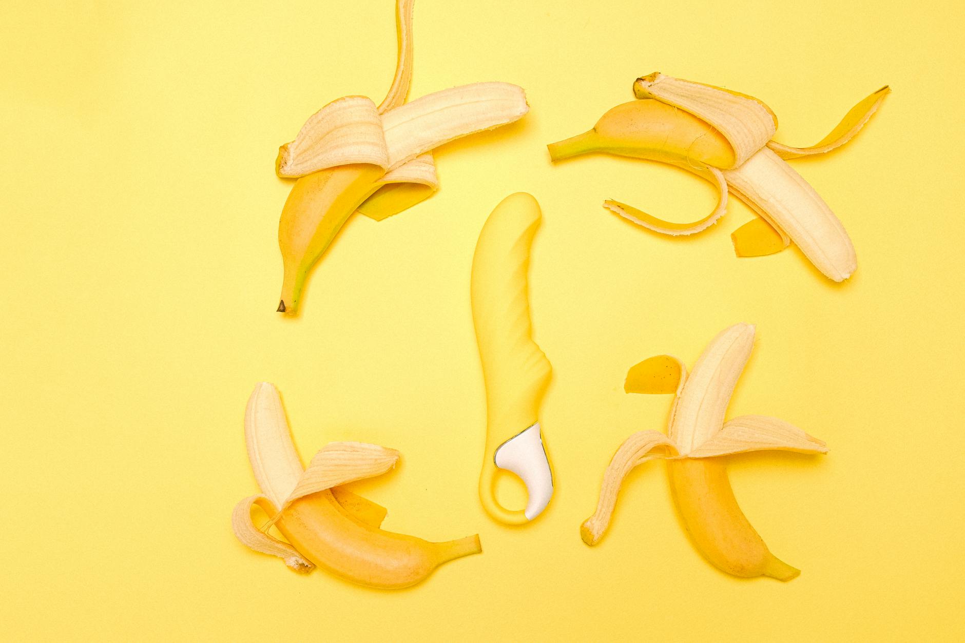 A sleek yellow lemon vibrator surrounded by fresh lemons on a bright yellow background