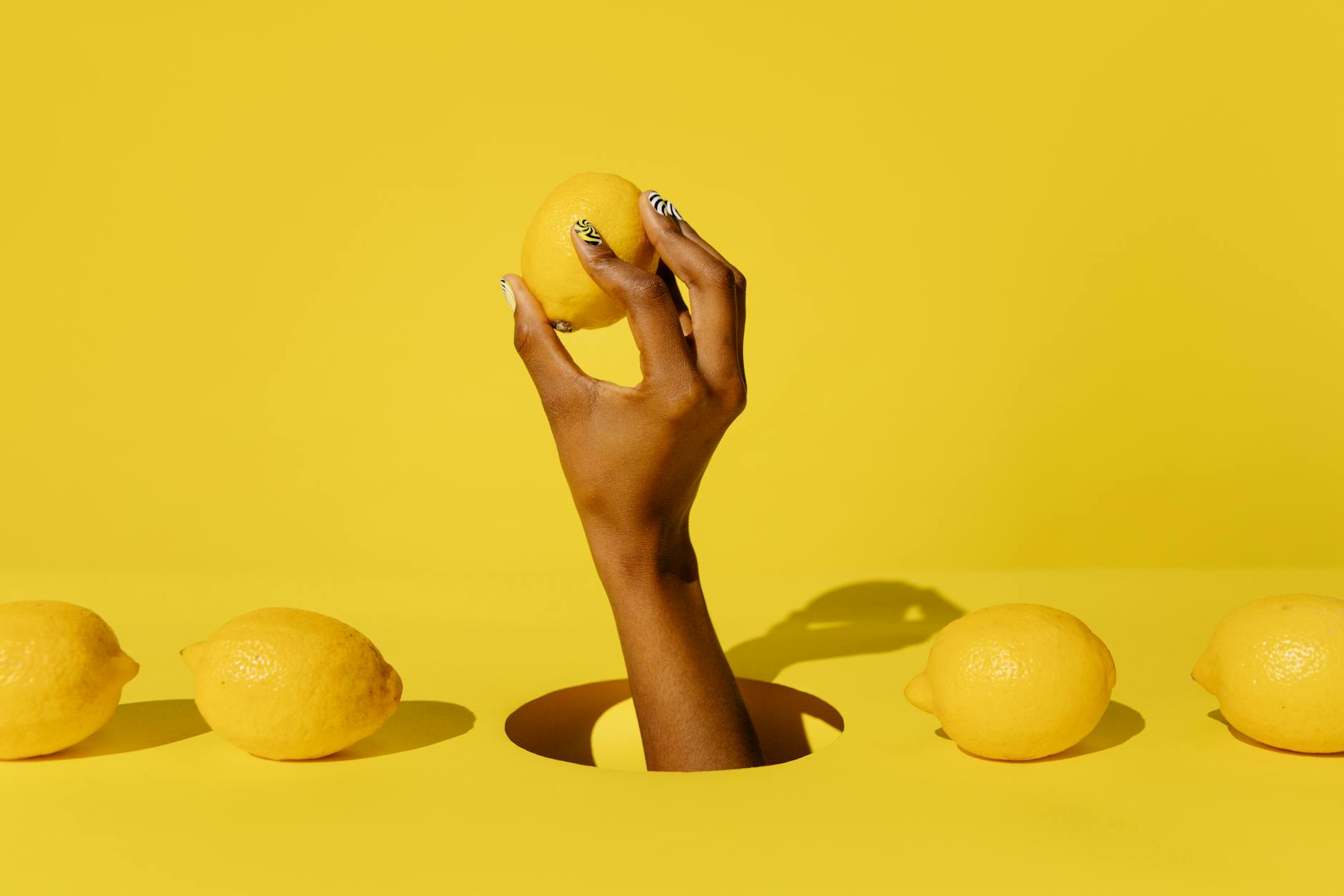 A fresh lemon held in a hand against a bright yellow background, symbolizing the gentle yet effective approach of lemon vibrators