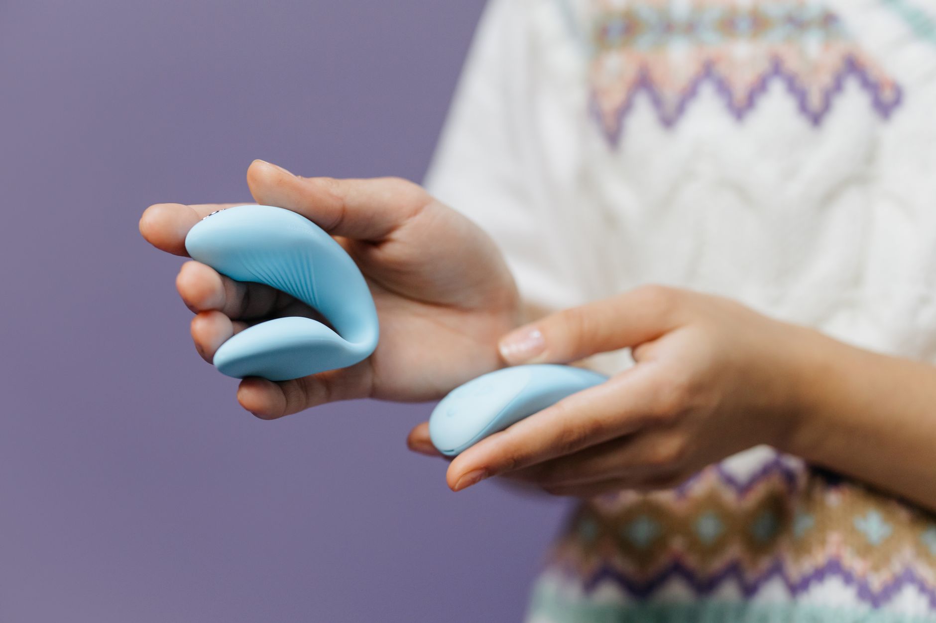 Close-up of hands holding a sleek lemon clitoral vibrator against a purple background