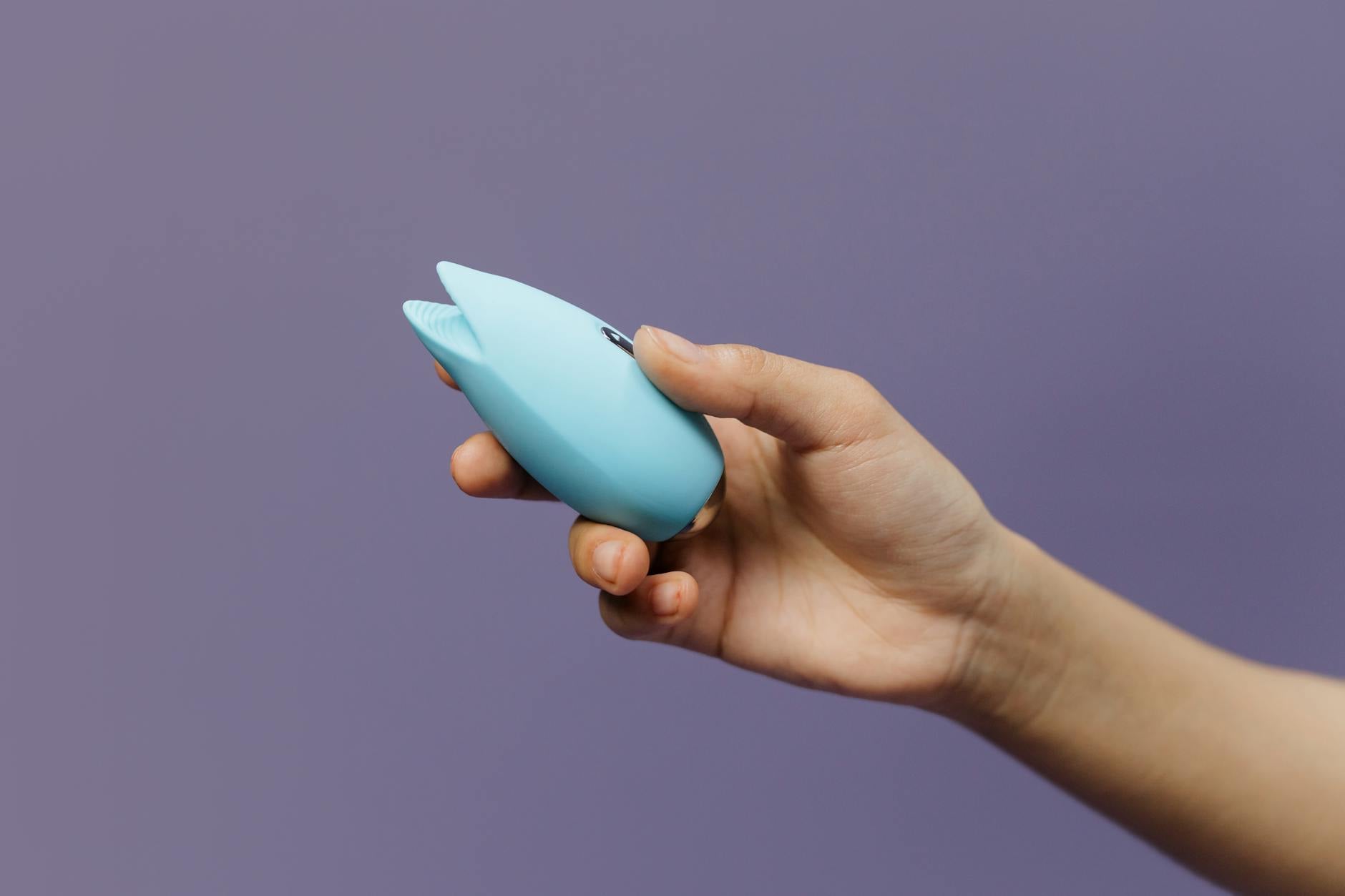 A blue silicone vibrator held in hand against a purple background, symbolizing self-care and reconnection with pleasure
