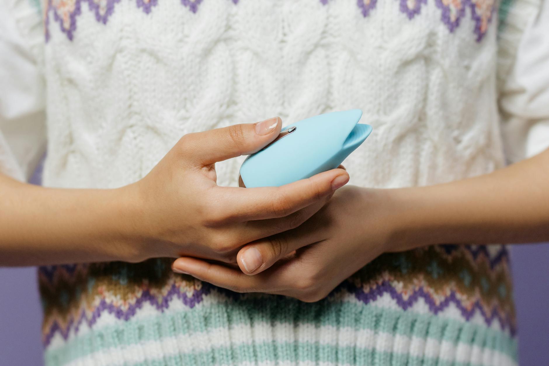 Hands holding a lemon clitoral vibrator against a knitted sweater