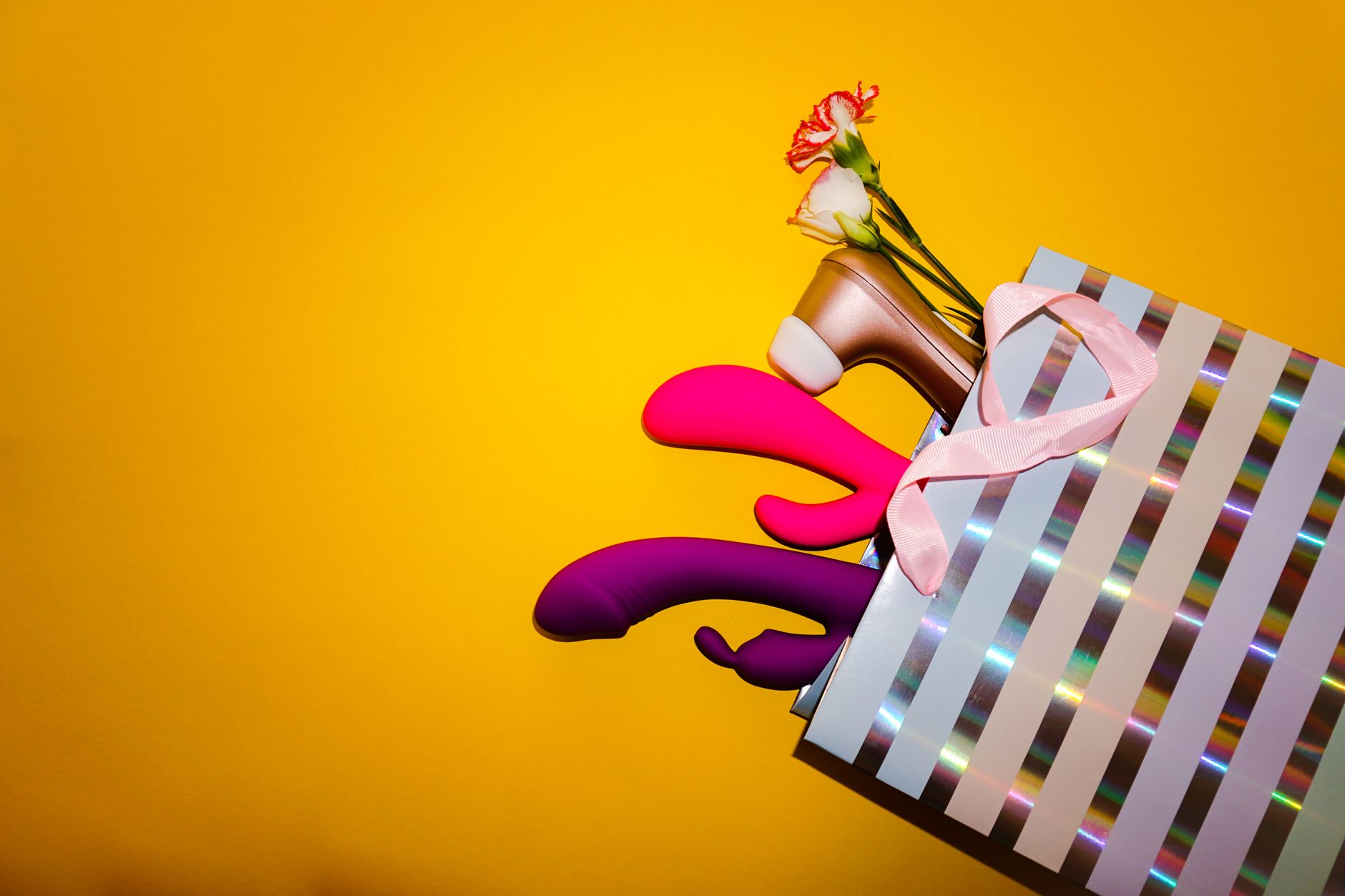 Colorful vibrators and lemon toys displayed with flowers in a gift arrangement against a bold yellow background